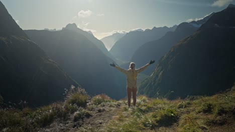 joyful woman putting hands in the air while looking at blissful mountain view