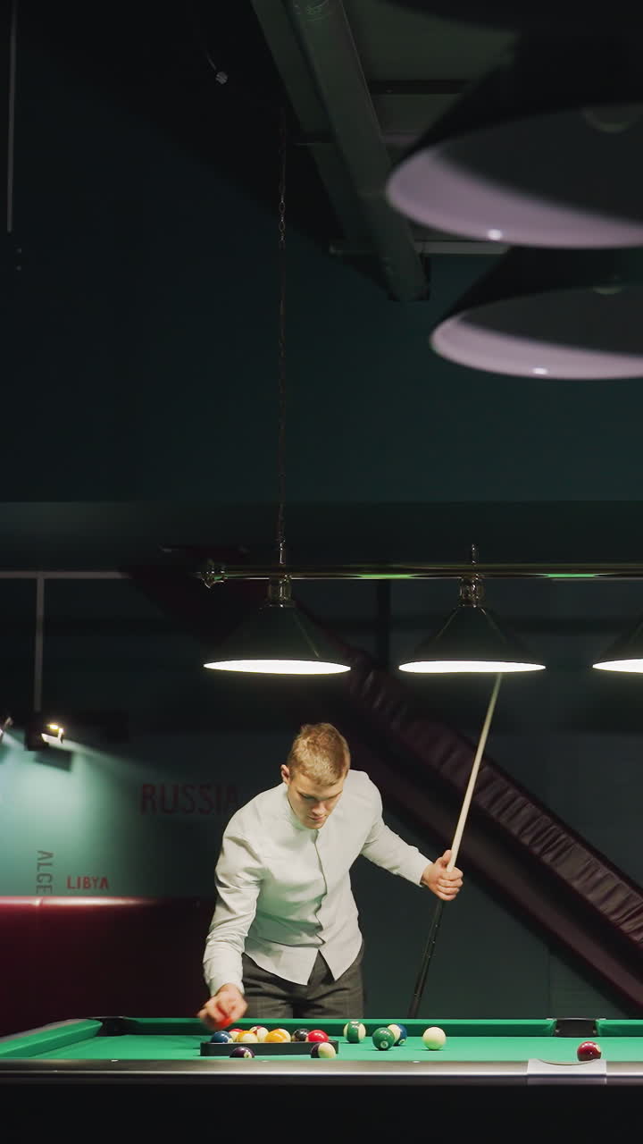 Giocatore di biliardo in camicia bianca appoggiato al tavolo da biliardo verde, che sistema le bilie a triangolo, preparandosi al tiro in una sala da biliardo con illuminazione soffusa e atmosfera rilassata