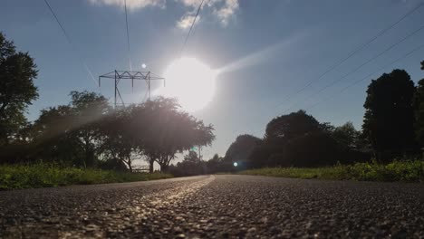 Tiefaufnahme-Eines-Gepflasterten-Radwegs-Mit-Der-Sonne-Im-Hintergrund-Und-Bäumen-Mit-Stromleitungen-Darüber