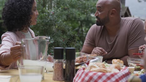 Feliz-Pareja-Birracial-Disfrutando-De-La-Comida-Y-Hablando-En-La-Mesa-En-El-Jardín,-Cámara-Lenta