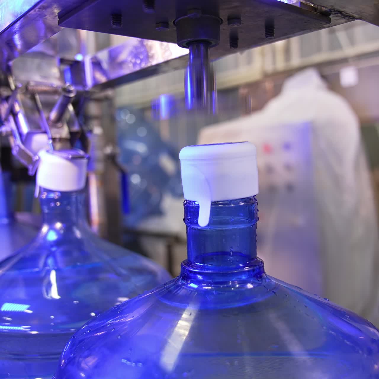 Corking the bottles of fresh clean water. Big flasks filled with water move by the conveyor belt. Mineral water production at factory