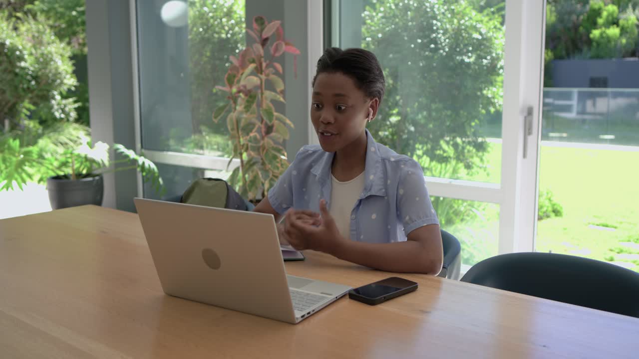African American teenager sitting at home table earbuds hearing laptop ping cheering checking notes