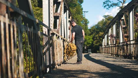 young man traveler with backpack arriving on rusty old bridge to admire the nature outdoors on sunny summer day