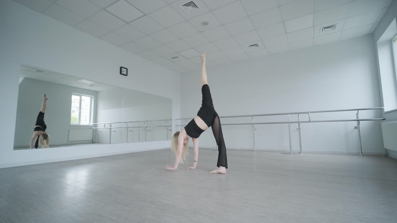 Ballerina in abiti neri che esegue danza contemporanea. Movimenti fluidi e aggraziati in una stanza bianca. Coreografia di balletto moderno.