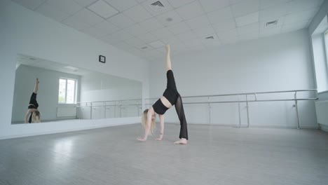 chica en forma con ropa negra actuando contemporáneamente. bailarina muestra movimientos fluidos, cuerpo y manos ondas en la habitación blanca. coreografía de danza de ballet moderno. joven se mueve suavemente