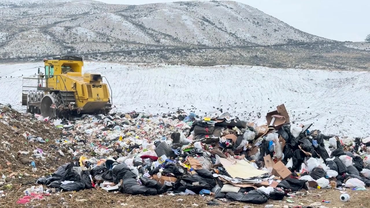 Handheld shot of a landfill compactor operating amidst a large pile of garbage at Dufferin Hill, Kamloops, with clear, balanced framing and natural lighting.