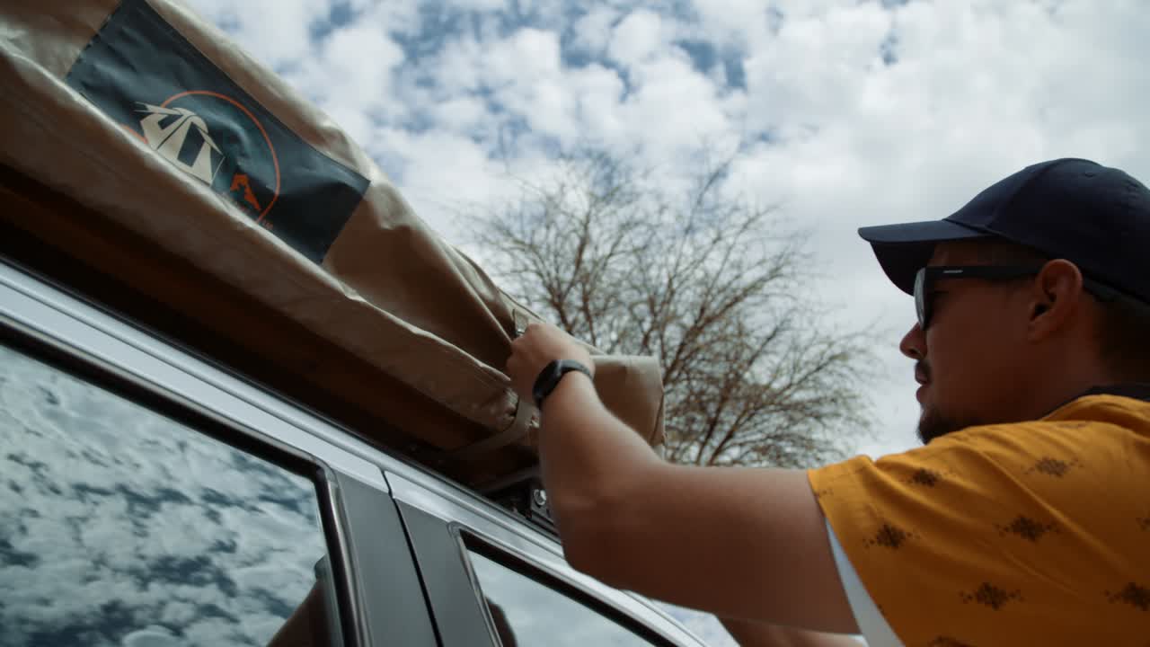Hand held shot of an off-roading Caucasian male tourist in Africa tying and securing his rooftop tent