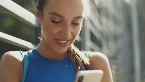 primer plano de un bonito mensaje de texto de deportista en el teléfono inteligente y sonriendo en la cancha al aire libre en un día de verano