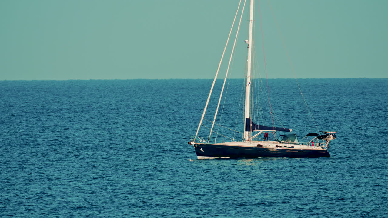A sleek sailboat anchored on calm open water, gently drifting under a clear turquoise sky