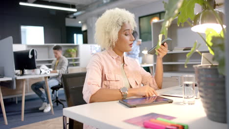 using smartphone and laptop, woman working in modern office environment
