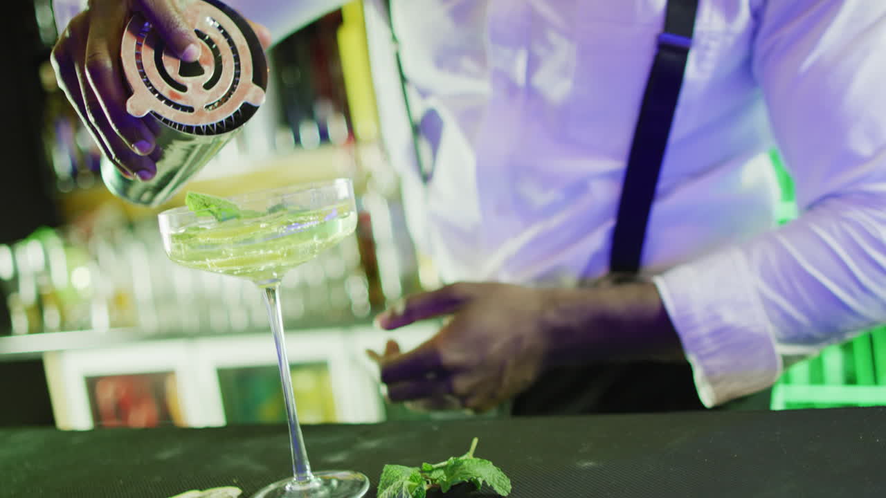 Video del busto di un barman afroamericano che prepara un cocktail verde al bar.