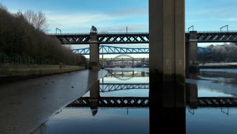 Hermoso-Reflejo-De-Los-Puentes-Sobre-El-Río-Tyne,-Newcastle-Mientras-Nos-Desplazamos-Detrás-Del-Montante-Vertical-Del-Puente-Redheugh.