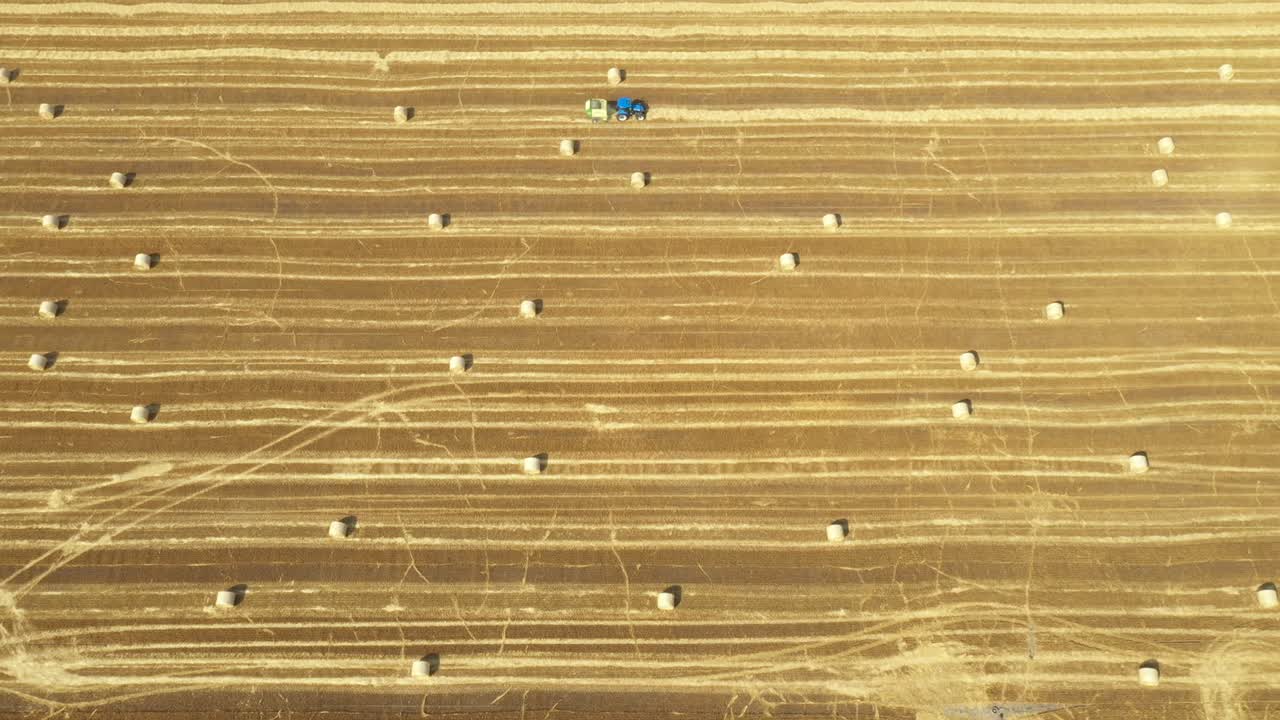 Aerial view of tractor tow trailed bale machine to collect straw from harvested field