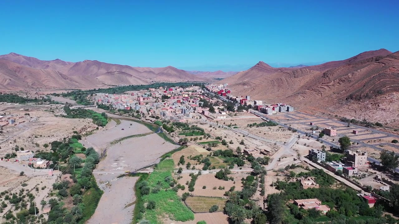 Ouarzazate vahası vadisinin drone havadan görünümü; verimli tarım arazilerinin Atlas Dağları ile buluştuğu, güneydoğu Fas'ın doğal güzelliğini ve kültürel manzaralarını sergileyen bir görüntü