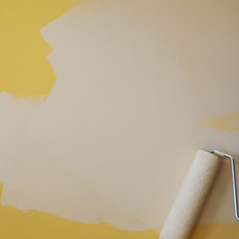 roller painting yellow wall with creamy paint. hand of a worker doing renovation the room with light color. close-up. makeover concept