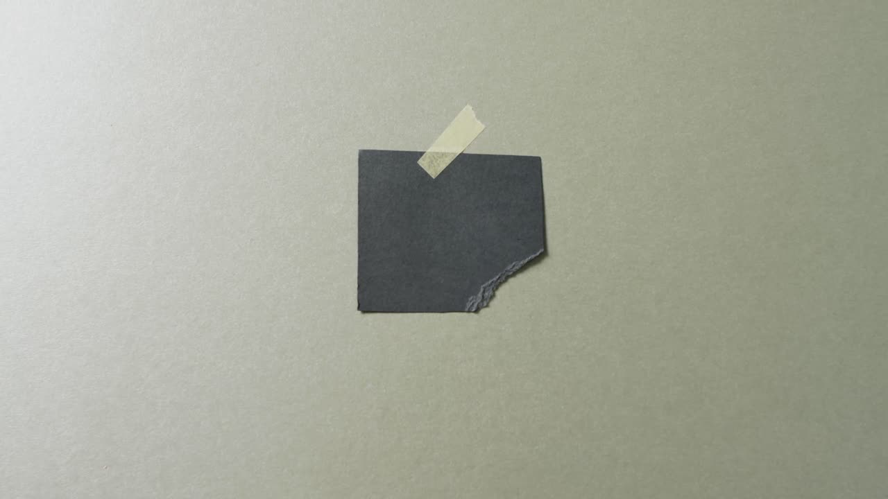 Video of close up of torn piece of black paper taped on green background