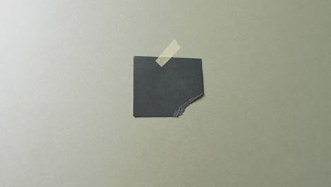 Video-of-close-up-of-torn-piece-of-black-paper-taped-on-green-background