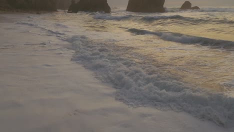 aerial view tilting over waves clos to rocky cliffs on atlantic ocean at the ursa beach, cloudy sunset in portugal