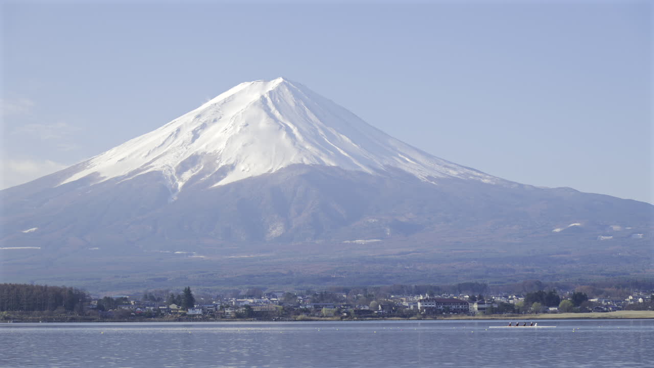 Mount Fuji stands proudly against the sky, showcasing its snow-covered summit. Surrounding landscapes and calm waters create a serene atmosphere, inviting exploration and admiration. Kawaguchiko Lake