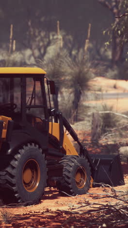 a yellow backhoe loader parked on a dirt road in a forest