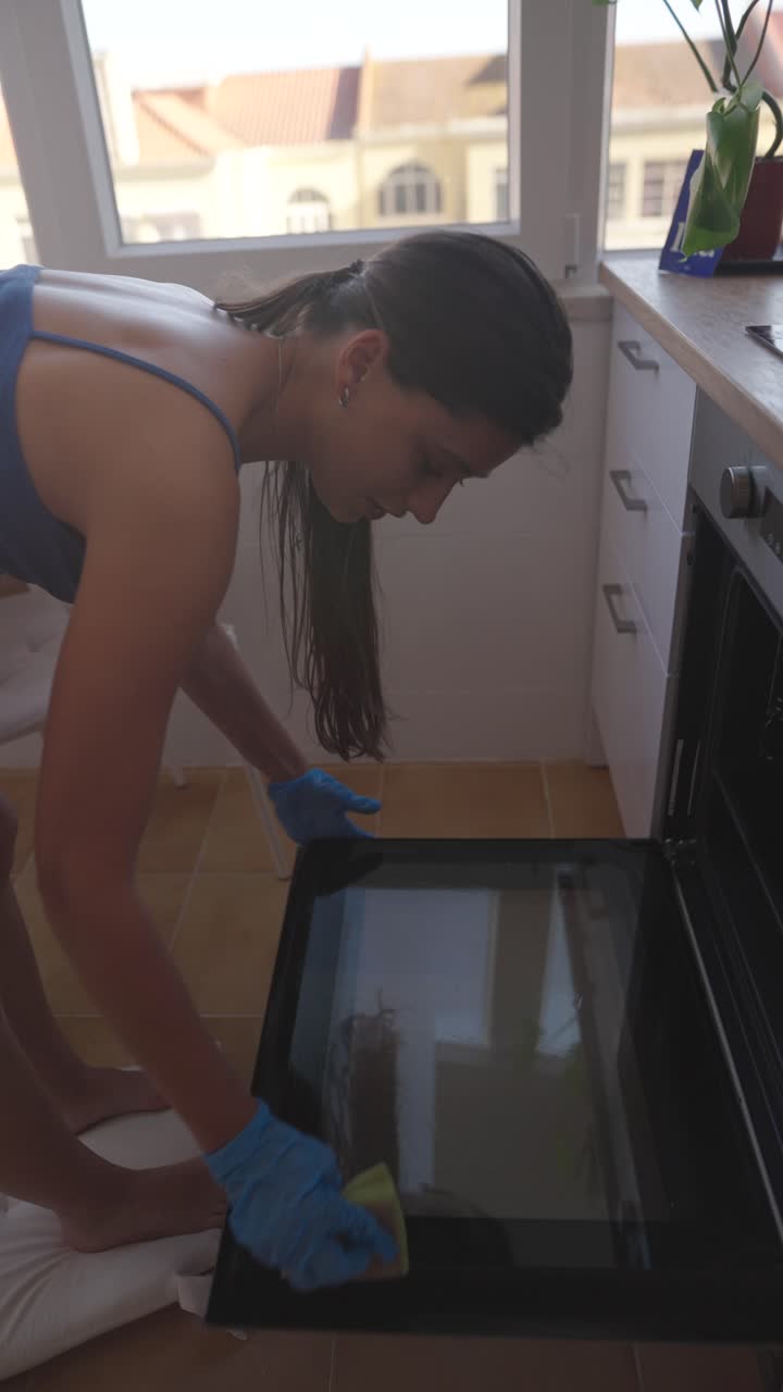 Giovane donna che pulisce lo sportello del forno in una cucina luminosa