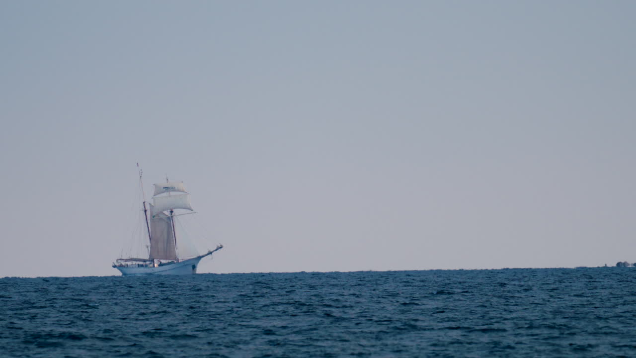 A majestic sailing ship appears on the horizon against a pastel sky and deep blue sea