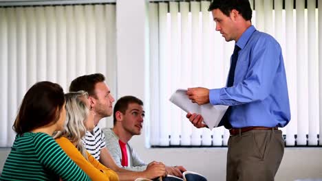 Lecturer-handing-out-assignments-to-his-students-in-classroom