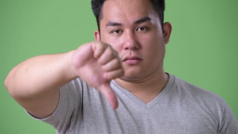 young handsome overweight asian man against green background