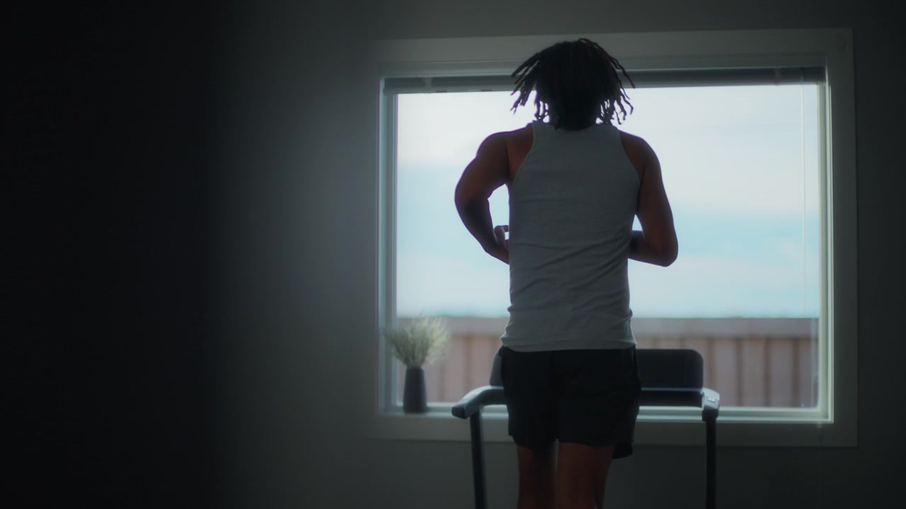 Young man with dreadlocks running on a treadmill in front of a window
