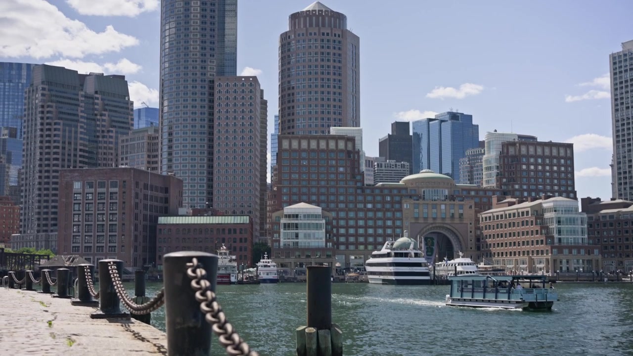 Carrellata cinematografica verso l'alto e panoramica a sinistra attraverso il porto di Boston con una pesante catena portuale in primo piano che rivela lo skyline del centro di Boston. Sole splendente e viste tranquille sul lungomare.