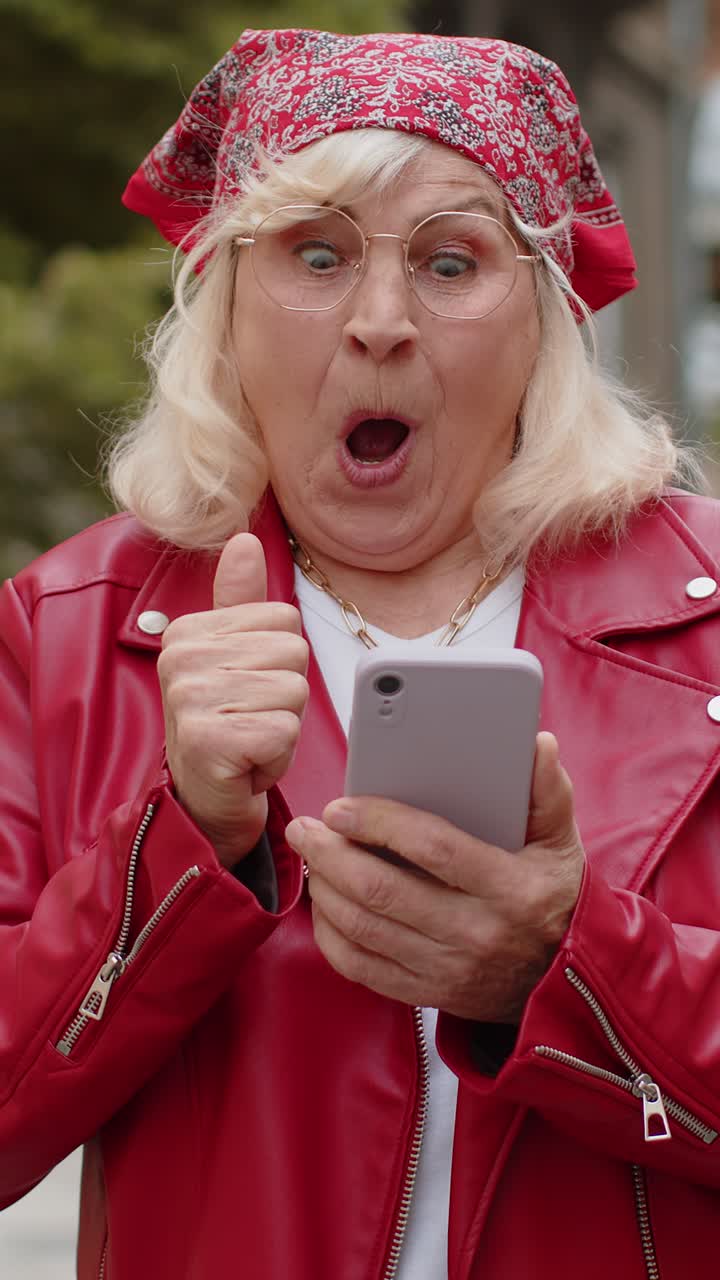 Eccitata felice vincitrice donna anziana usa lo smartphone per festeggiare la vittoria buone notizie per le strade della città