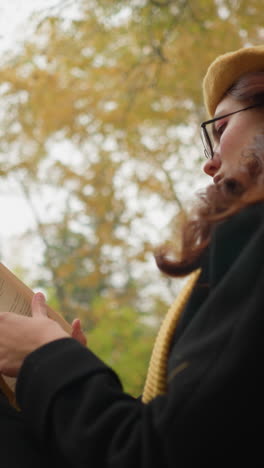 lower angle view of woman in yellow beret with red hair cascading down her shoulder as she carefully opens a page of her book, immersed in deep thought