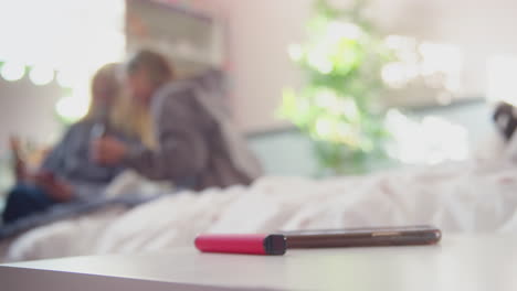 dos adolescentes en el dormitorio bebiendo botellas de cerveza con un bolígrafo de vape en primer plano