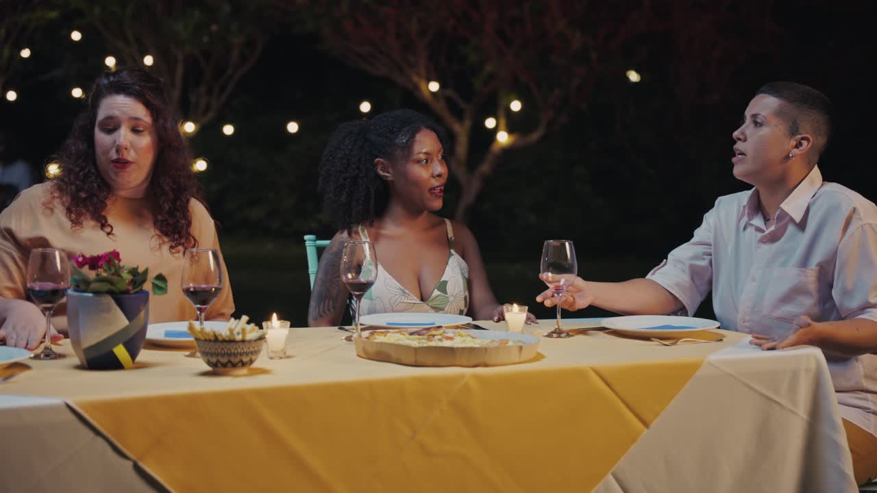 Friends enjoying an outdoor dinner party with wine and food at night under string lights
