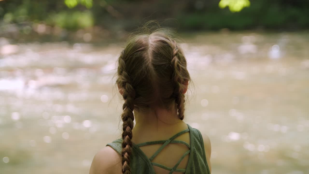 tiro por encima del hombro de una niña arrojando un palo a un río