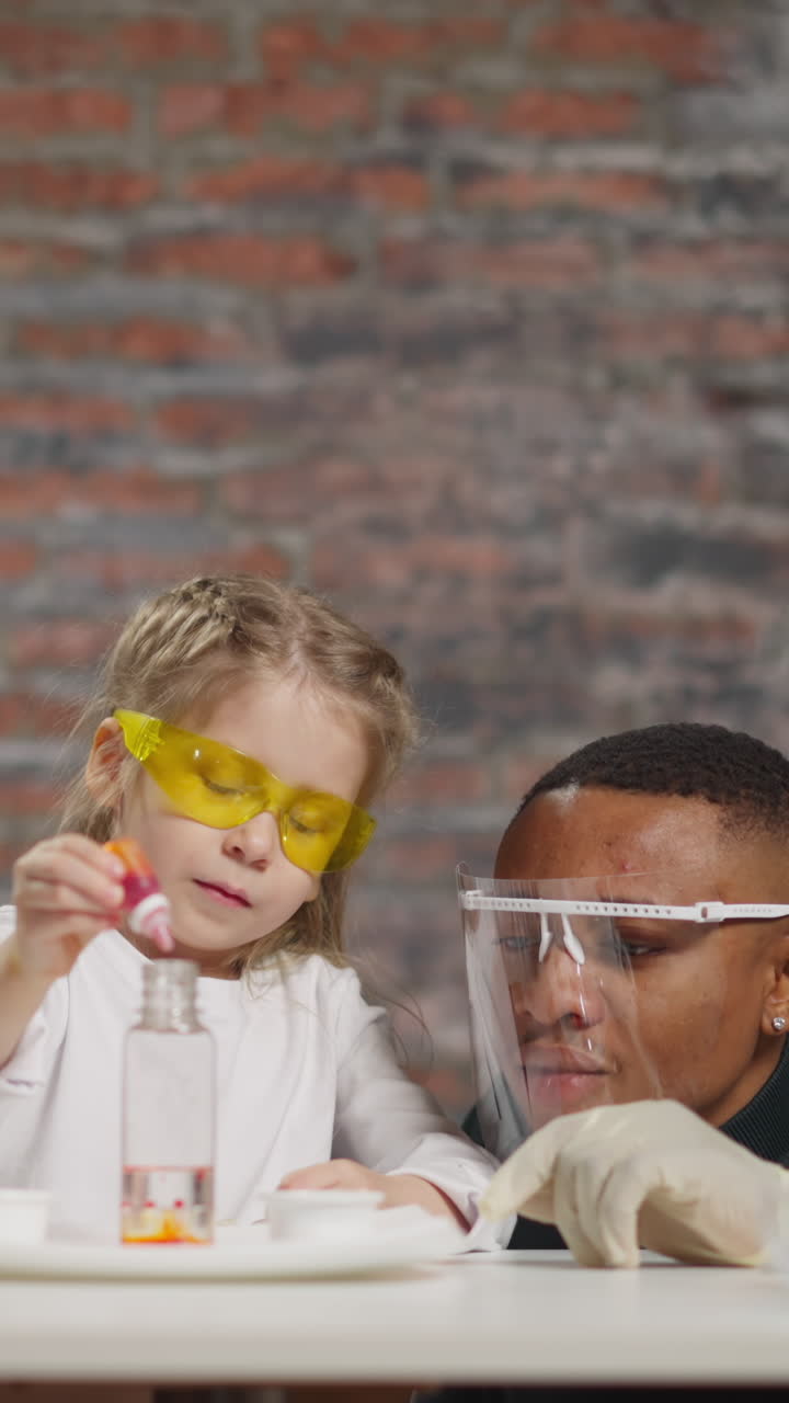 Pretty little girl with Asian and African-American scientists does experiment with liquid and paint at fun science lesson in laboratory