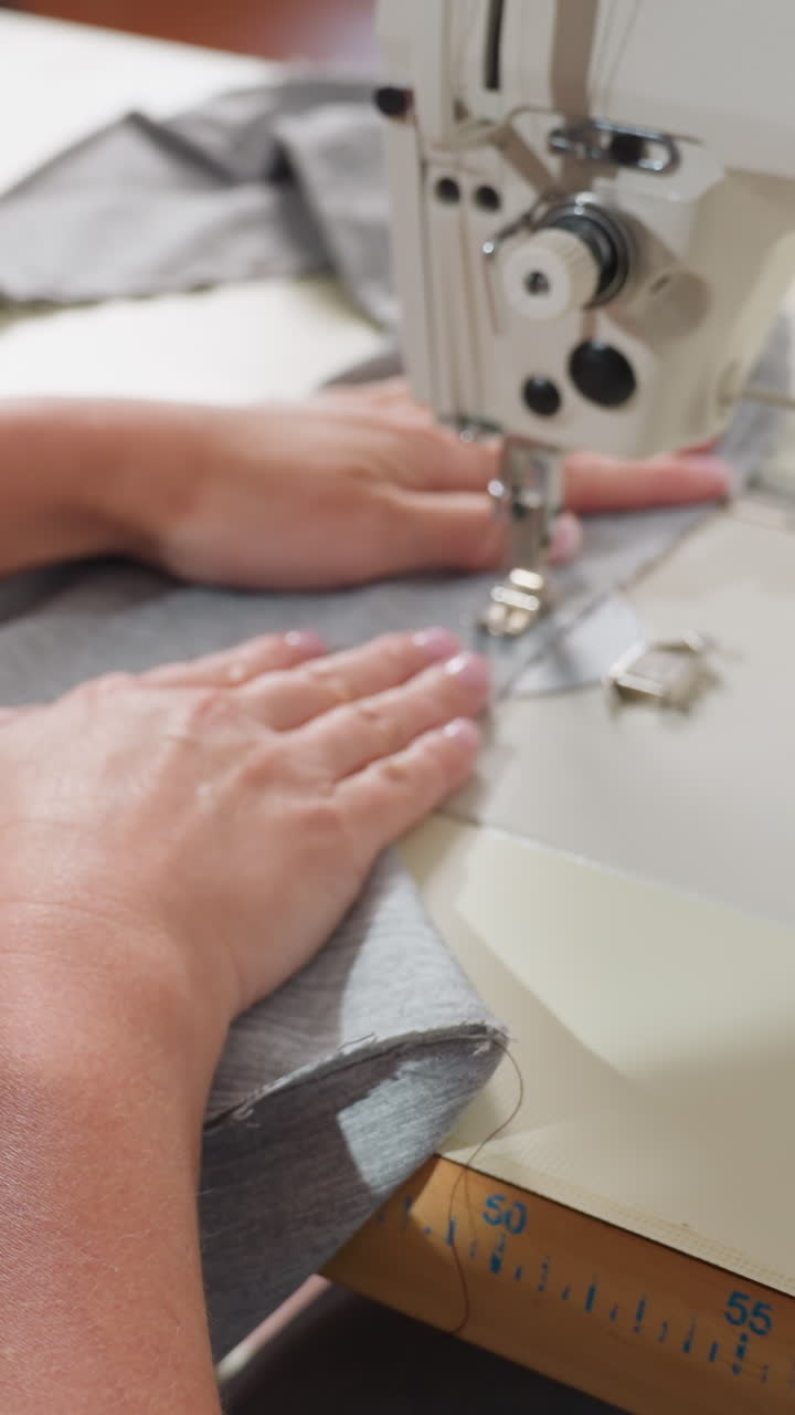 Worker operating sewing machine carefully, Skilled worker guiding fabric with precision, Caucasian operator expertly guides grey fabric through industrial sewing machine with steady hands