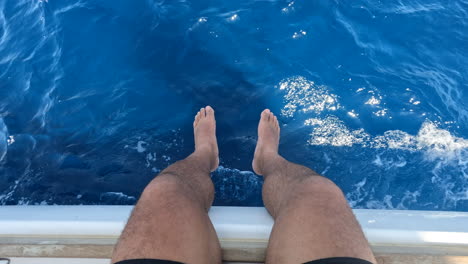 Male-legs-hanging-over-the-side-of-a-moving-boat-over-the-water