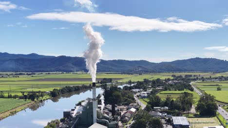 aerial footage of a sugar mill with smoke rising, set against a lush, rural landscape under clear skies