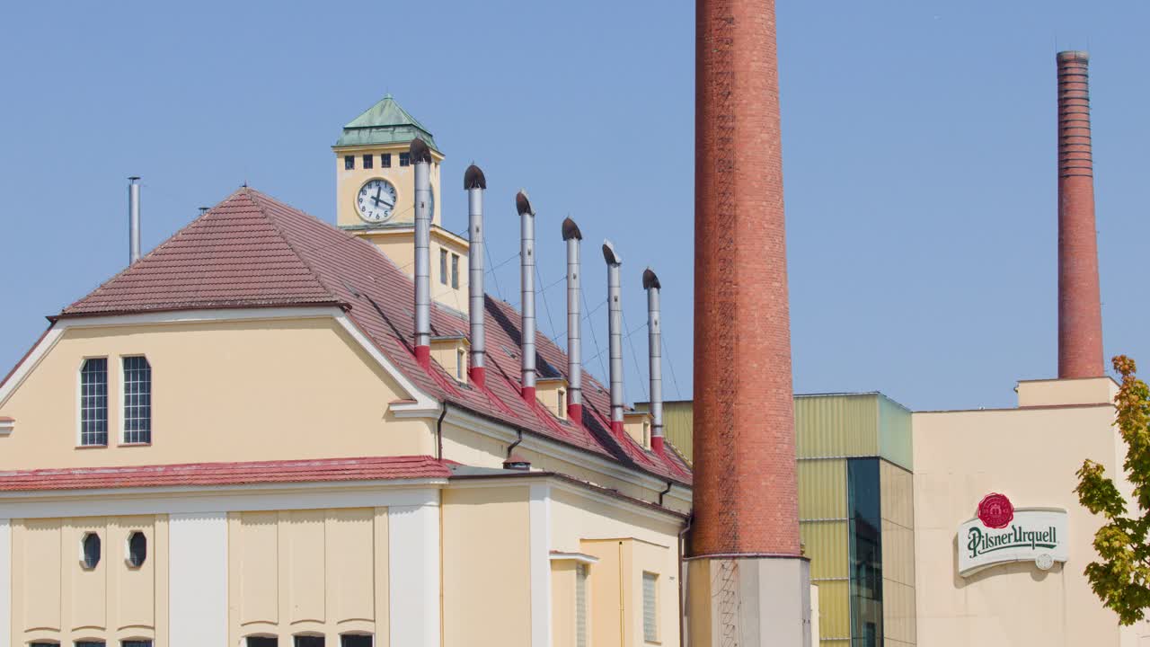 Sunny view of historic brewery buildings, tall chimneys, and clocktower against clear blue sky