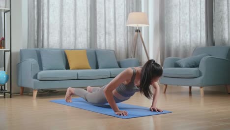 mujer asiática sana con ropa deportiva entrenando en una alfombra de yoga, haciendo perro mirando hacia arriba durante el entrenamiento en casa