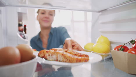 Mujer-Joven-Alcanzando-El-Interior-Del-Refrigerador-De-Comida-Saludable-Para-Salmón-Fresco-En-El-Plato