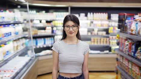 portrait of attractive young asian woman standing in supermarket with shelves of dairy on background, looking at camera and