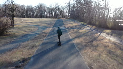 an aerial tracking of a man on an electric skateboard in an empty park on a sunny day