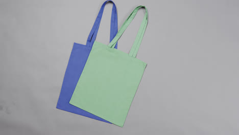 Close-up-of-blue-and-green-bags-on-grey-background,-with-copy-space,-slow-motion