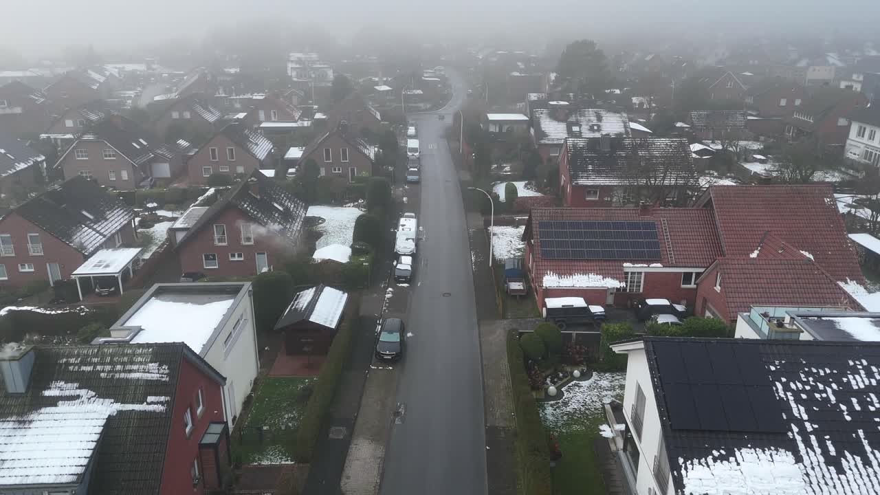 Aerial flyover street of German small town during snowy and foggy day. Red brick houses and homes with solar panels on rooftop. Wide shot.