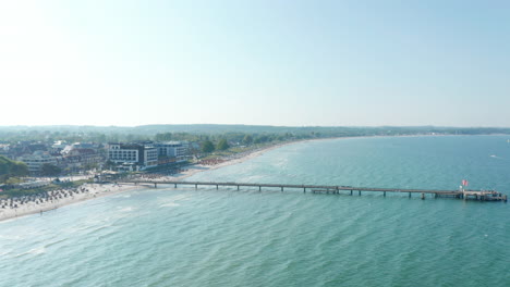 Aerial-drone-view-flying-above-Baltic-sea-pier-beach-in-Scharbeutz,-Germany,-summer-sunny-day,-circle-pan