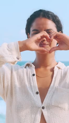woman forms love symbol with hands at the beach on a sunny day