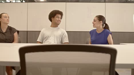 african american male, arab american female and caucasian female in their 20's in a meeting with video moving right to left with chairs in the foreground