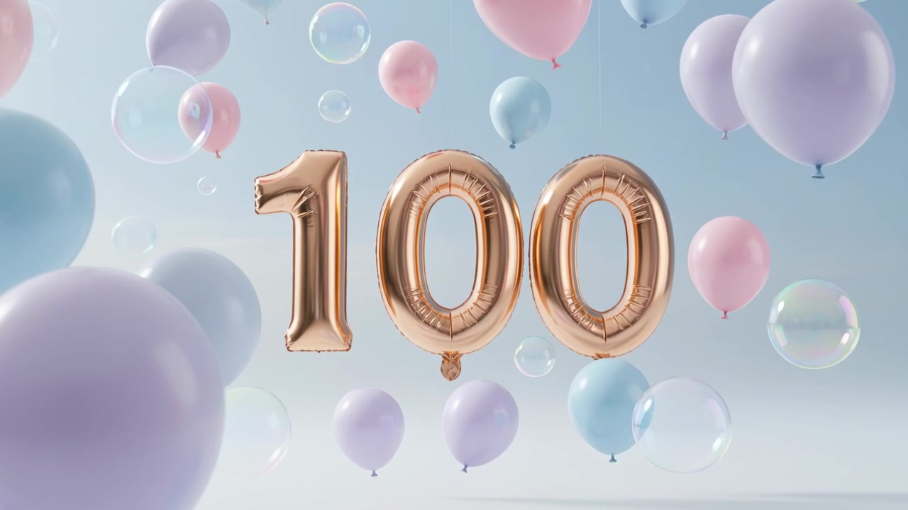 La telecamera zooma rivelando un numero 100 color oro rosa che ondeggia in studio, con palloncini pastello e bolle che segnano un traguardo.